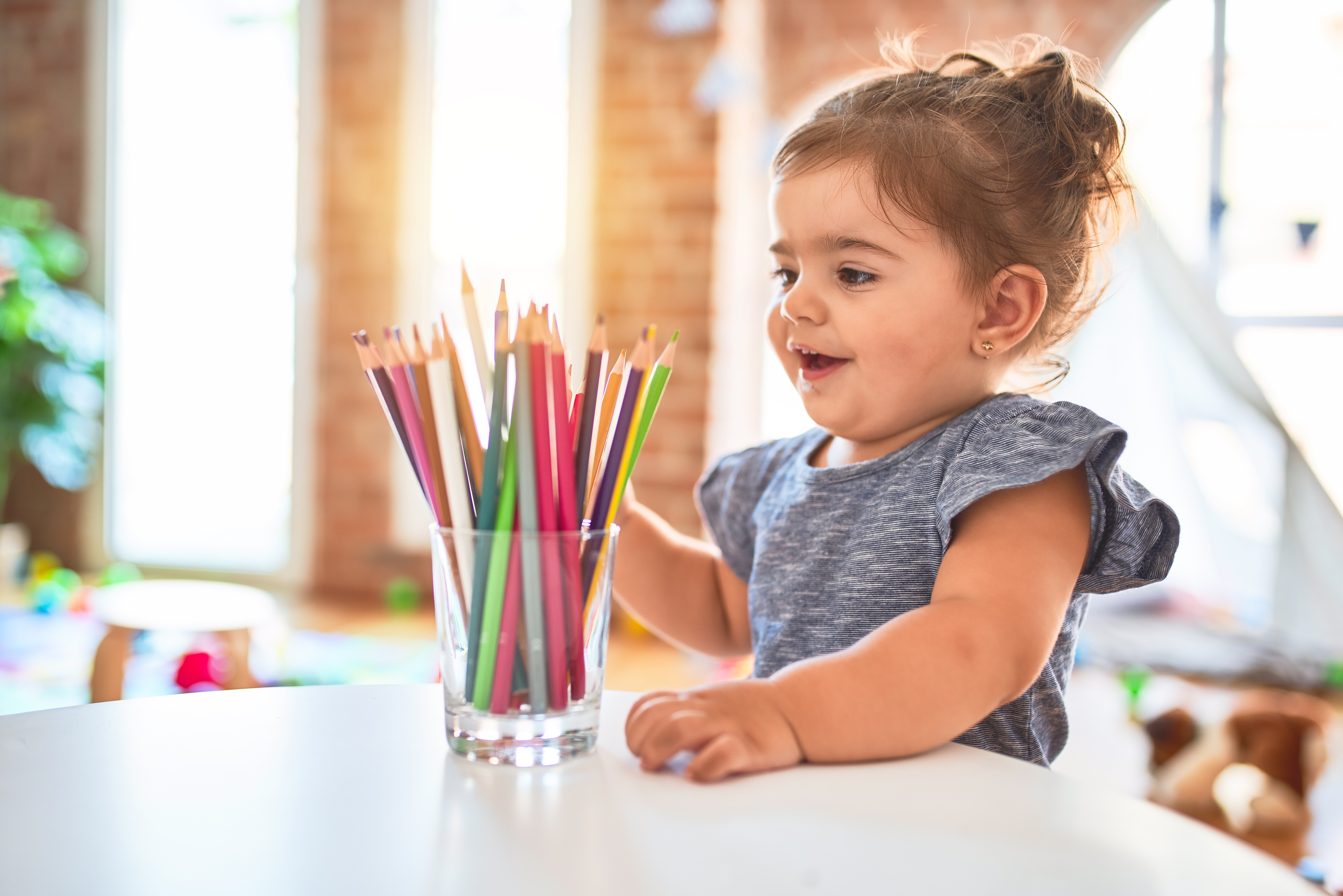 Beautiful toddler standing holding colored pencils at kindergarten